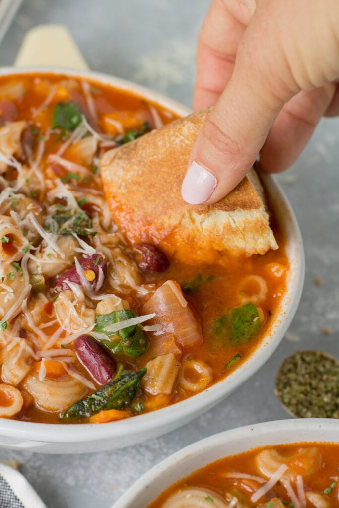 A piece of bread being dunked into Vegetarian Minestrone Soup
