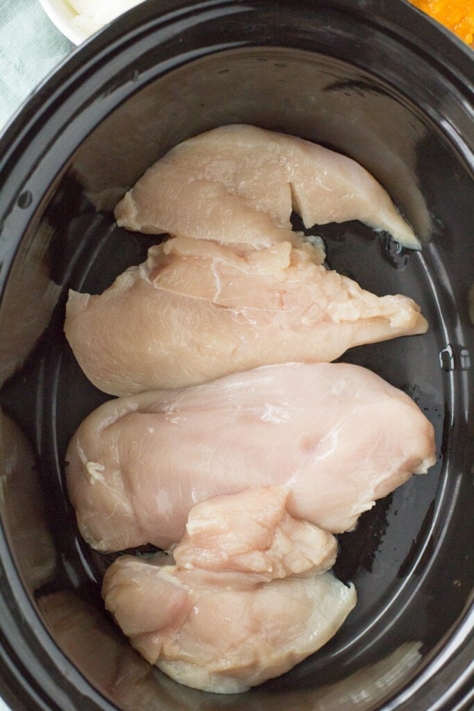 An overhead of chicken in a crockpot for pumpkin chicken chili