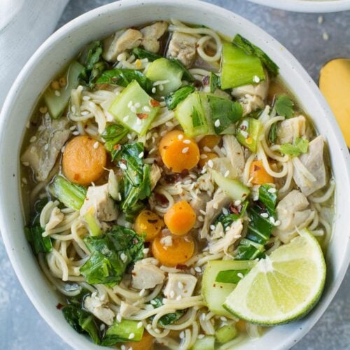 Asian Chicken Soup in a white bowl on a grey background with a gold spoon and linen off to the side