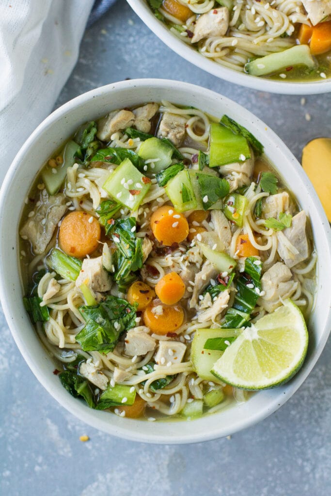 Asian Chicken Soup in a white bowl on a grey background with a gold spoon and linen off to the side