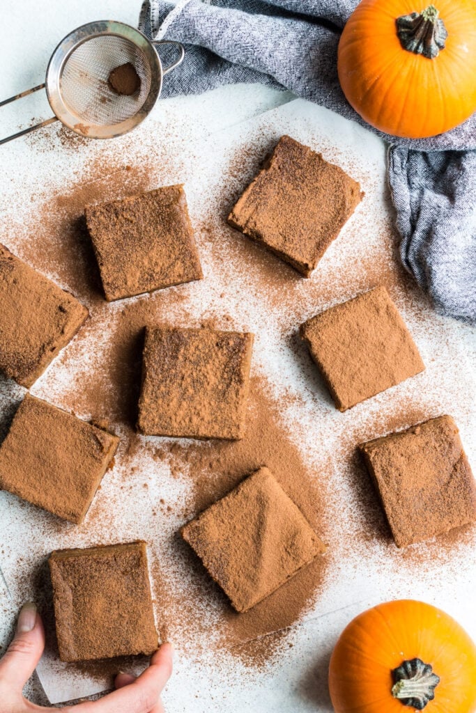 An overhead shot of pumpkin pie bars on a light background with pumpkins and cinnamon off to the side