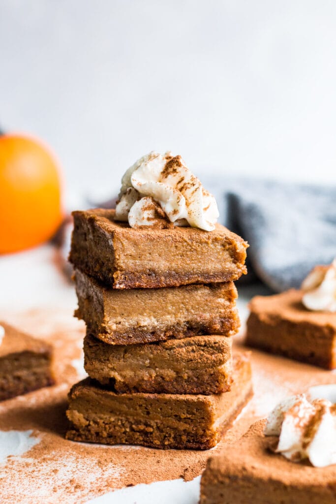 A close up of Healthy Pumpkin Pie Bars stacked together with pumpkins and linens in the background