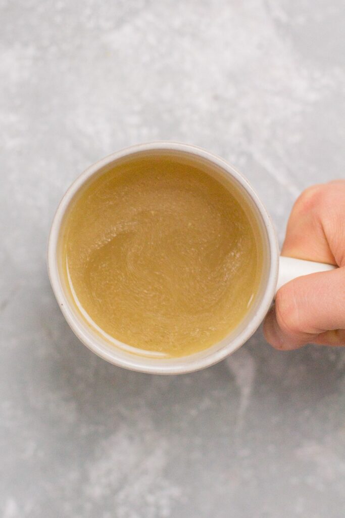A mug of turkey stock made in the crockpot on a grey background
