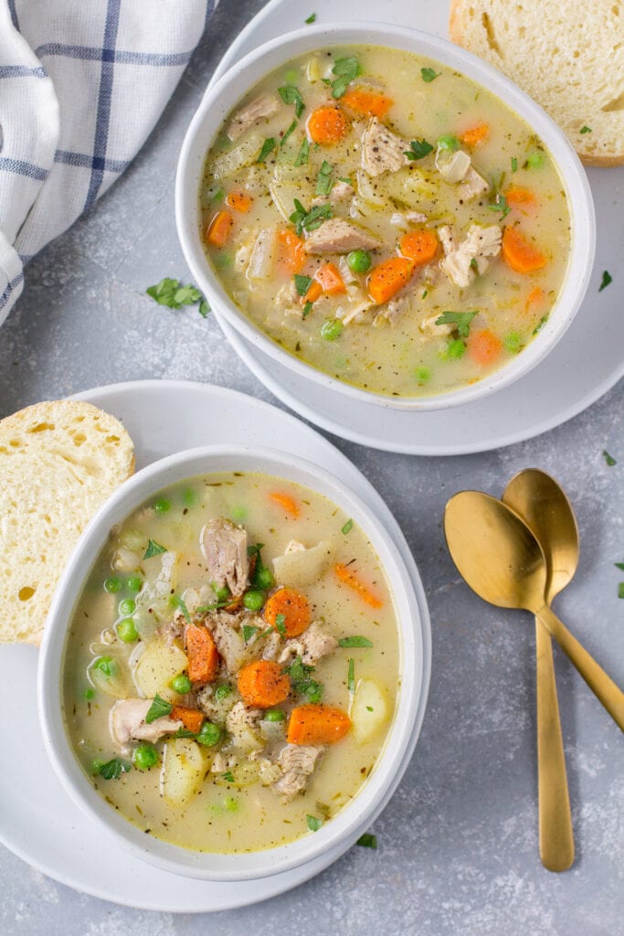An overhead image of two bowls of Turkey Pot Pie Soup with gold spoons and a blue linen off to the side
