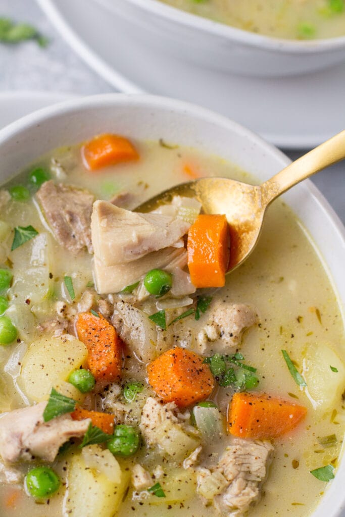 A bowl of healthy turkey soup with a gold spoon taking a bite out of it.
