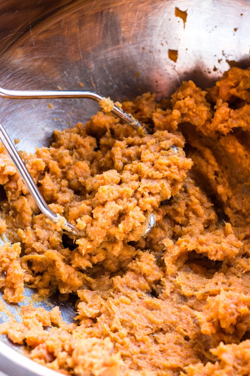 Mashed sweet potatoes in a bowl with a masher in it.