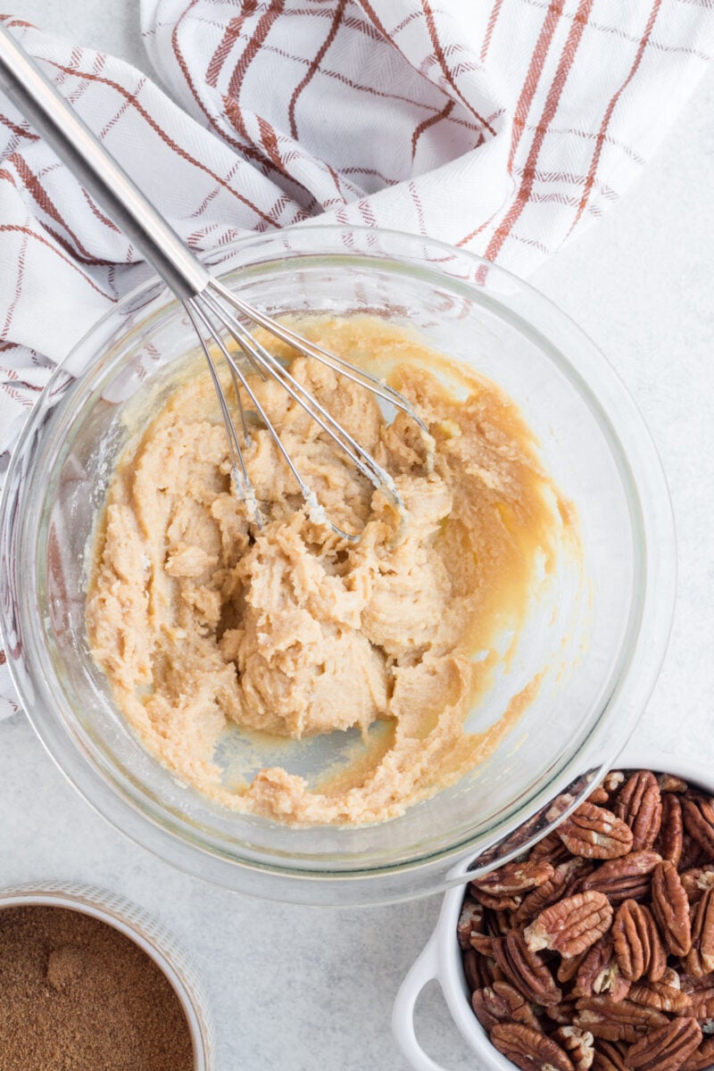 Pecan pie bar crust ingredients mixed together in a glass bowl with a whisk in the bowl.