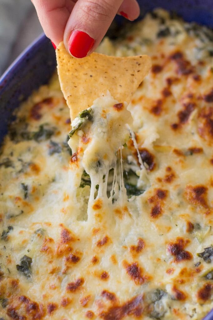 Healthy Spinach Artichoke Dip with a hand and a chip - a healthy christmas appetizer