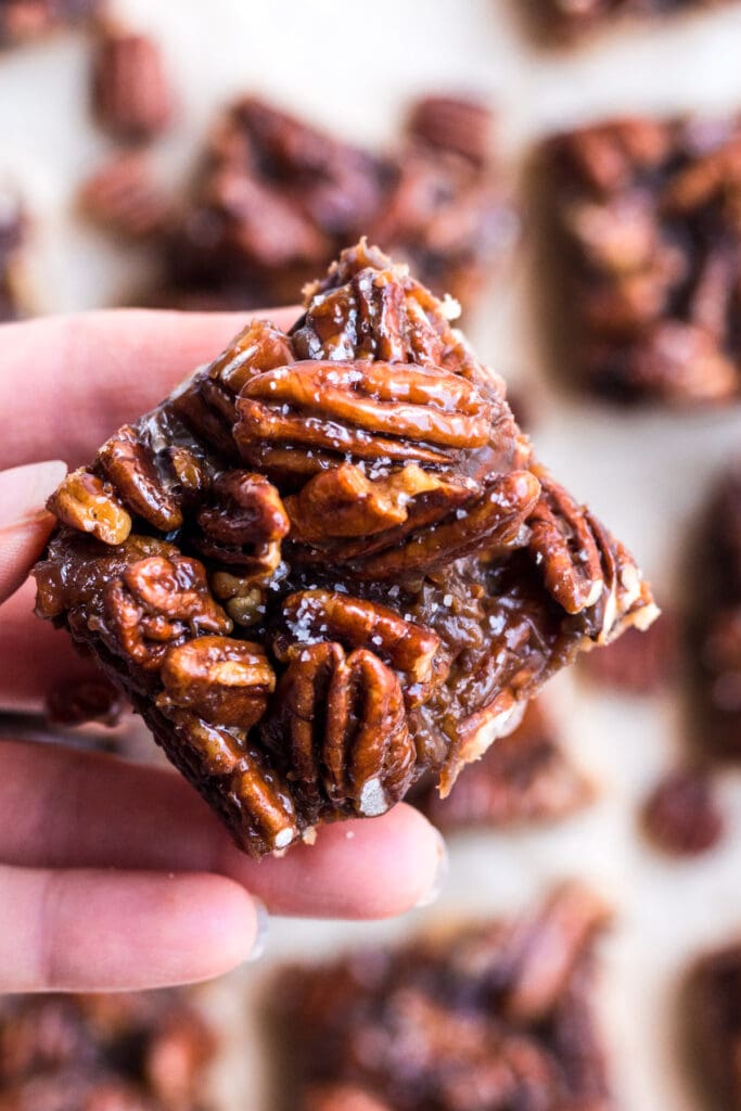 A hand holding a healthy pecan pie bar up to the camera