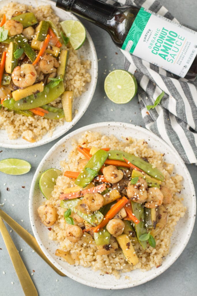 Gluten Free Shrimp Stir Fry on two plates with forks, a linen and coconut aminos off to the side.