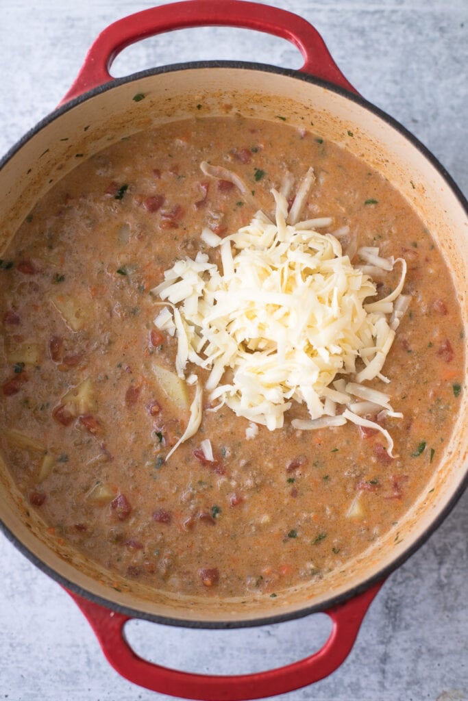 Cheeseburger Soup with cheese being stirred into the pot