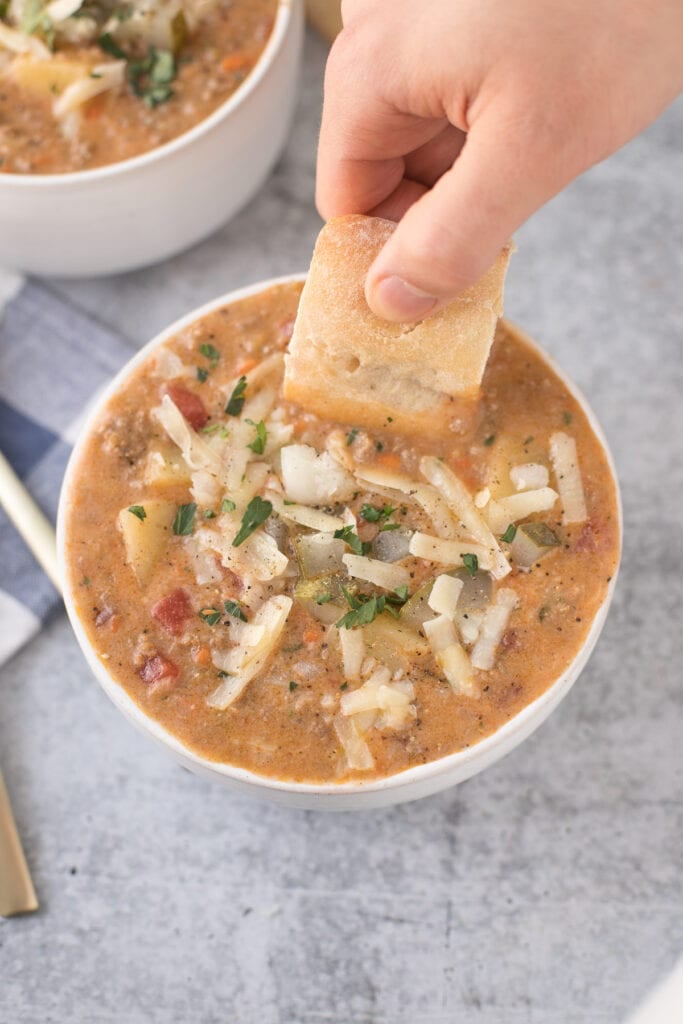 A piece of bread being dunked into Cheeseburger Soup