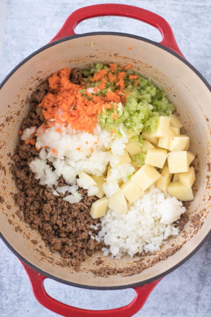 Cheeseburger Soup being cooked in a pot with veggies being added in