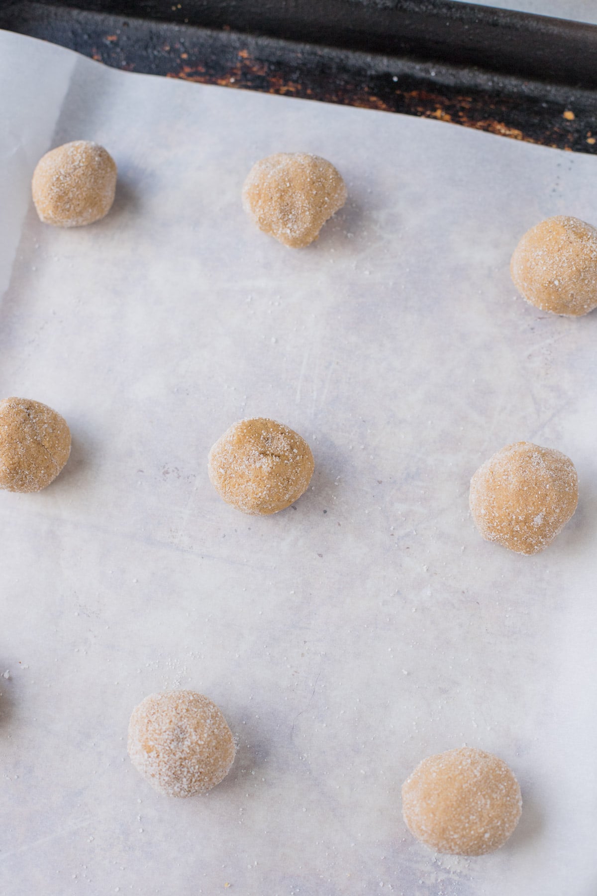 gingersnap cookies rolled in sugar on a parchment lined baking sheet before being baked