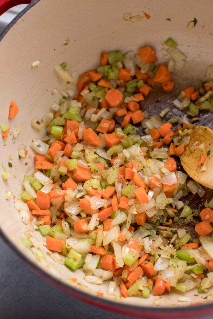 Veggies sauteing in a red dutch oven for ham potato soup