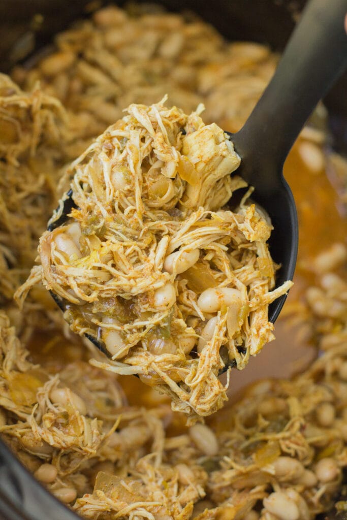 A close up view of healthy white chicken chili in a crockpot with a black ladle taking a scoop out