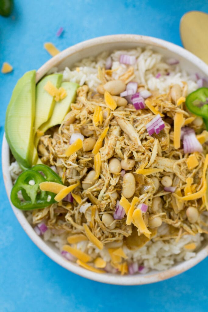 A close up of healthy chicken chili in a white bowl on a bright blue background
