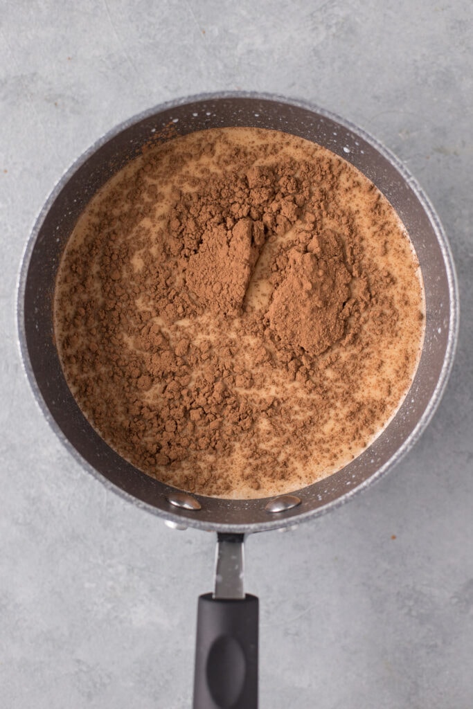 Cocoa powder and maple syrup being mixed in a pot for vegan hot cocoa