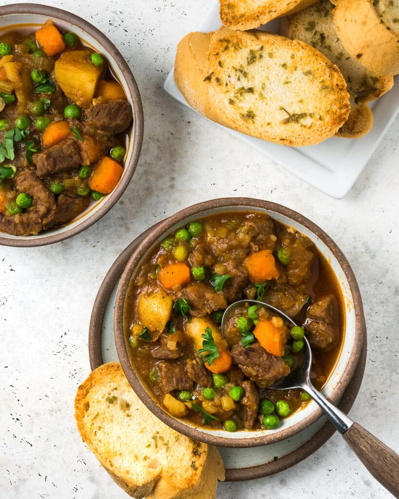 An above shot of two white bowls with beef stew with bread on the side on a white background