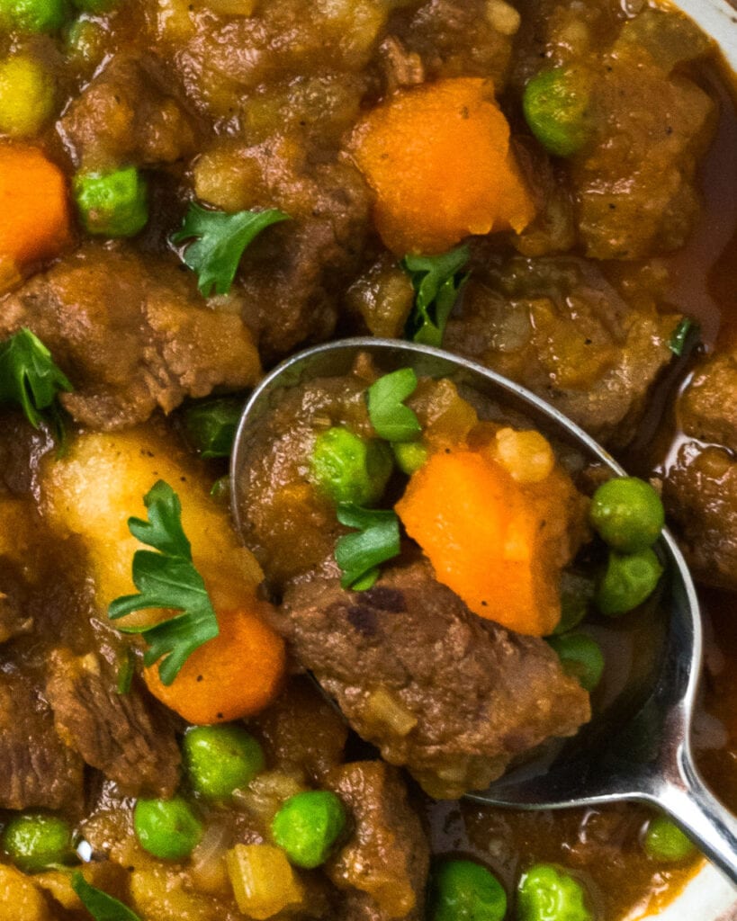 A closeup shot of instant pot beef stew with a silver spoon getting a bite