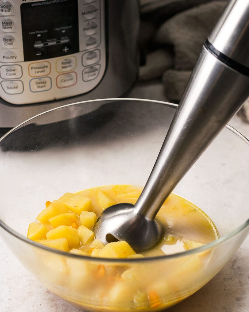An immersion blender in a bowl blending up instant pot potato soup