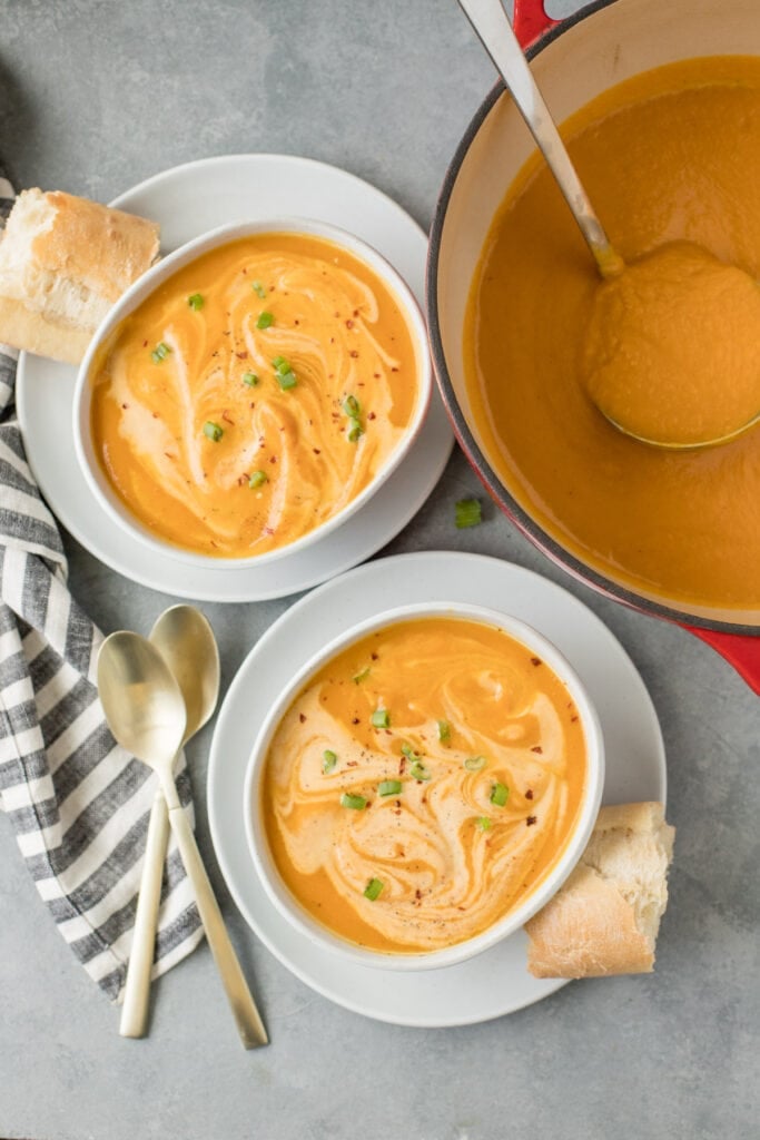 Two bowls of sweet potato soup and a dutch oven filled with sweet potato soup on a grey background