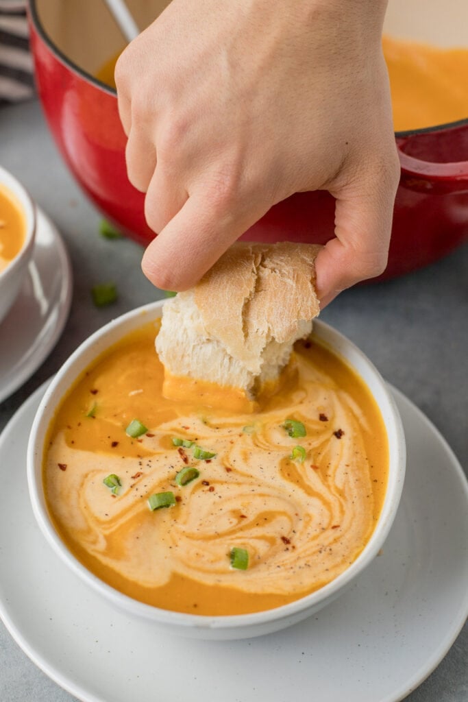A hand dunking a piece of bread into creamy sweet potato soup