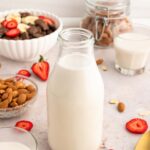 Whole30 Almond Milk in a glass milk bottle with almonds and strawberries on the side.