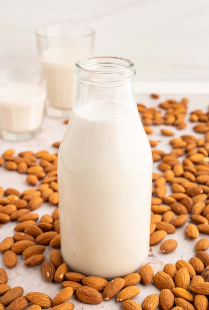 Homemade Almond Milk in a glass milk bottle surrounded with almonds.