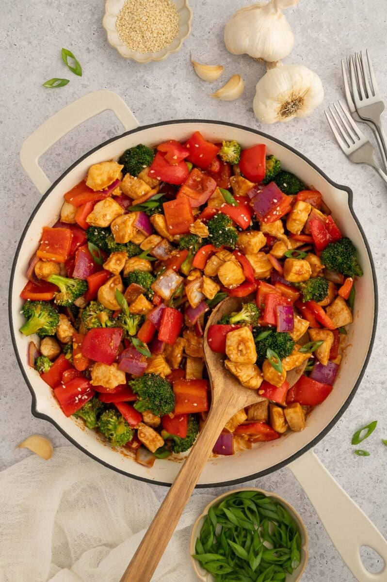 Healthy Sweet & Sour Chicken in a skillet with a wooden spoon in it.