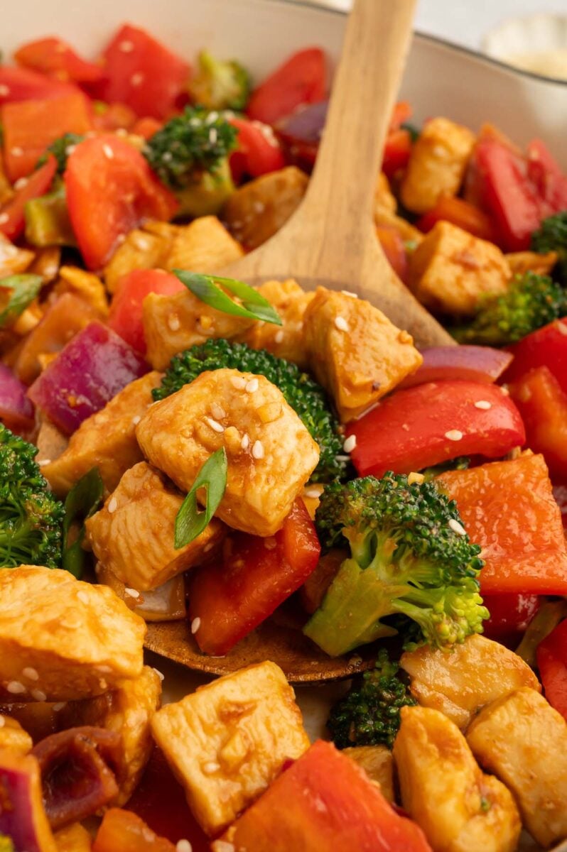 Healthy Sweet & Sour Chicken in a skillet with a wooden spoon in it.