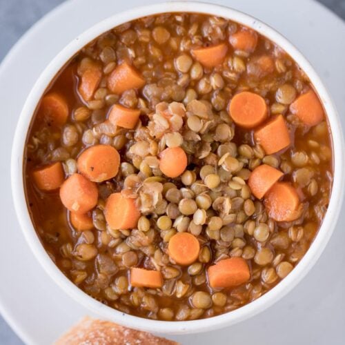 A bowl of easy lentil soup on a white plate with bread off to the side