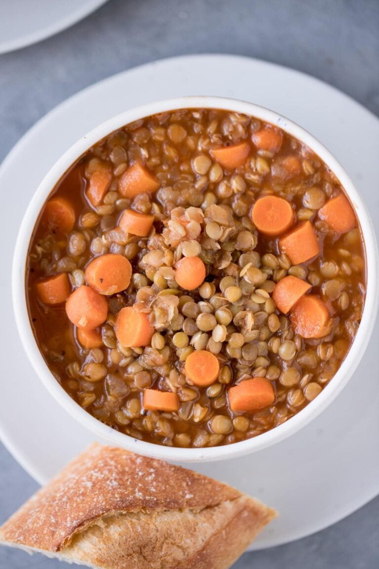 A bowl of easy lentil soup on a white plate with bread off to the side