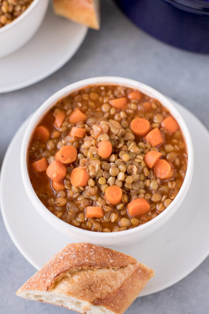 A bowl of easy lentil soup on a white plate with bread off to the side