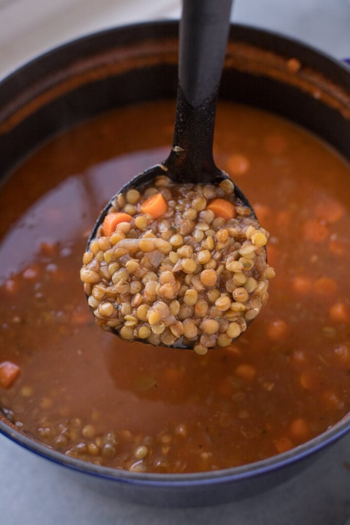 A ladle scooping out healthy lentil soup from a dutch oven