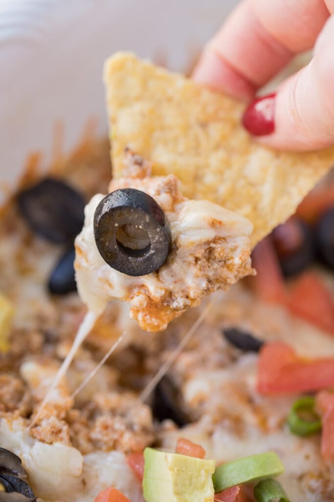 A chip taking a scoop out of taco dip with meat