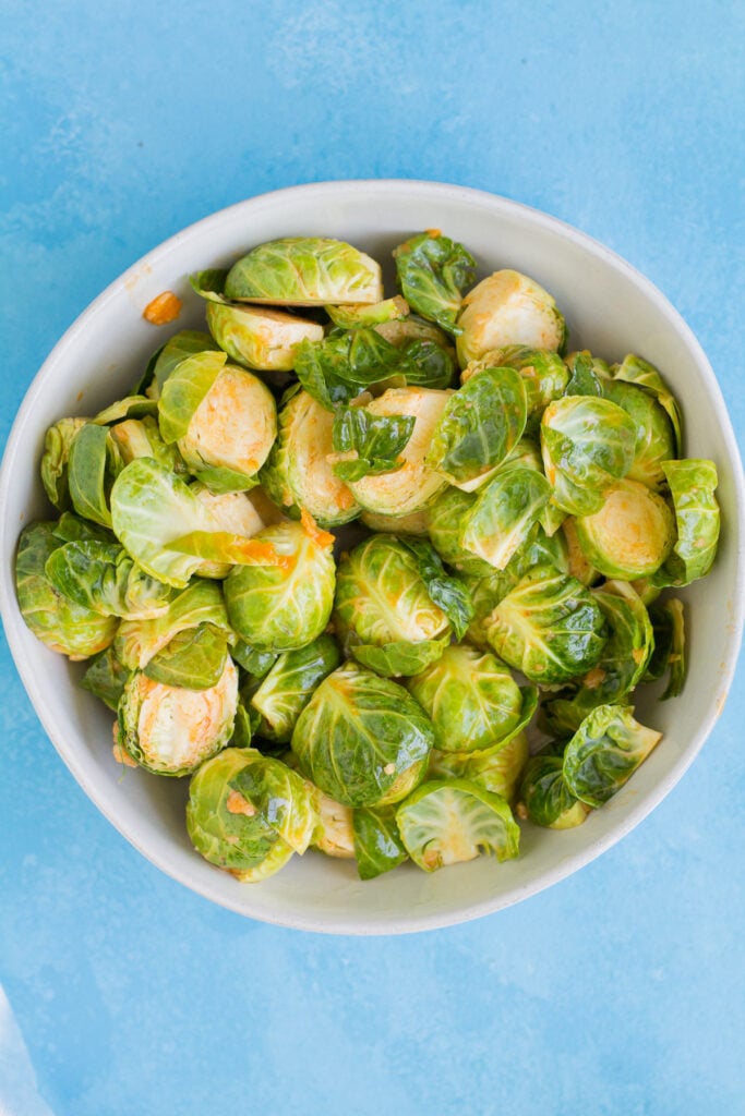 A bowl of brussels sprouts being tossed with buffalo sauce