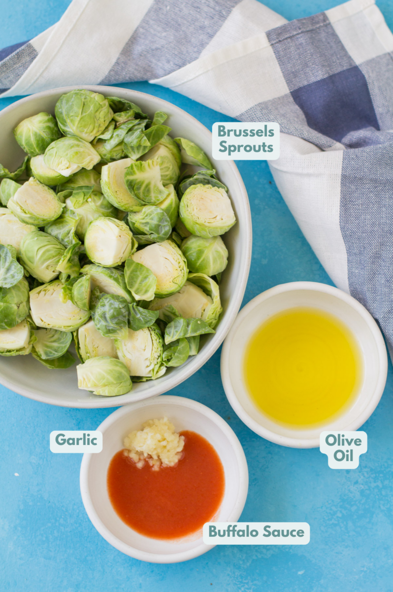 Ingredients for buffalo brussels sprouts in small white bowls on a blue background