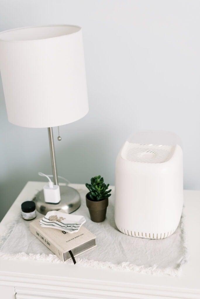 A canopy humidifier on a nightstand with a small plant, journal and lamp