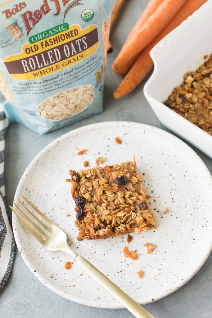 Carrot Cake Baked Oats on a white specked plate with a gold fork and a bag of oats off to the side
