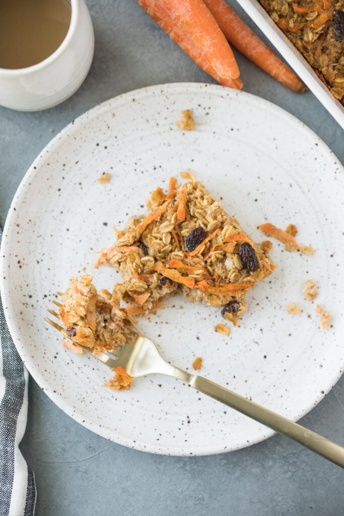 Baked Carrot Cake Oats on a white plate with a gold fork taking a bite out of the oatmeal