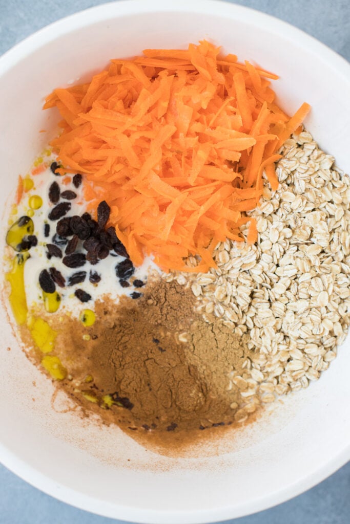 A white bowl filled with carrot cake oats ingredients before being stirred together