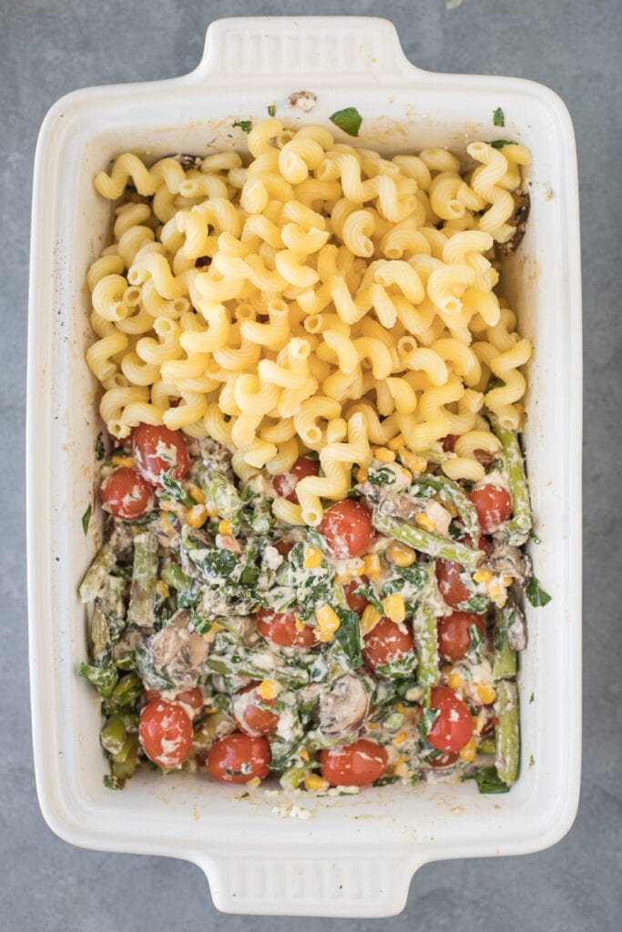 Pasta being added to baked feta and vegetables for easy feta pasta