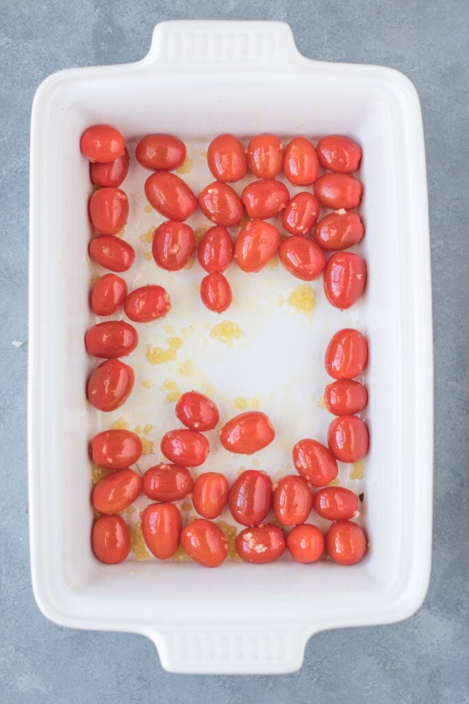 A white baking dish with cherry tomatoes, olive oil and garlic.