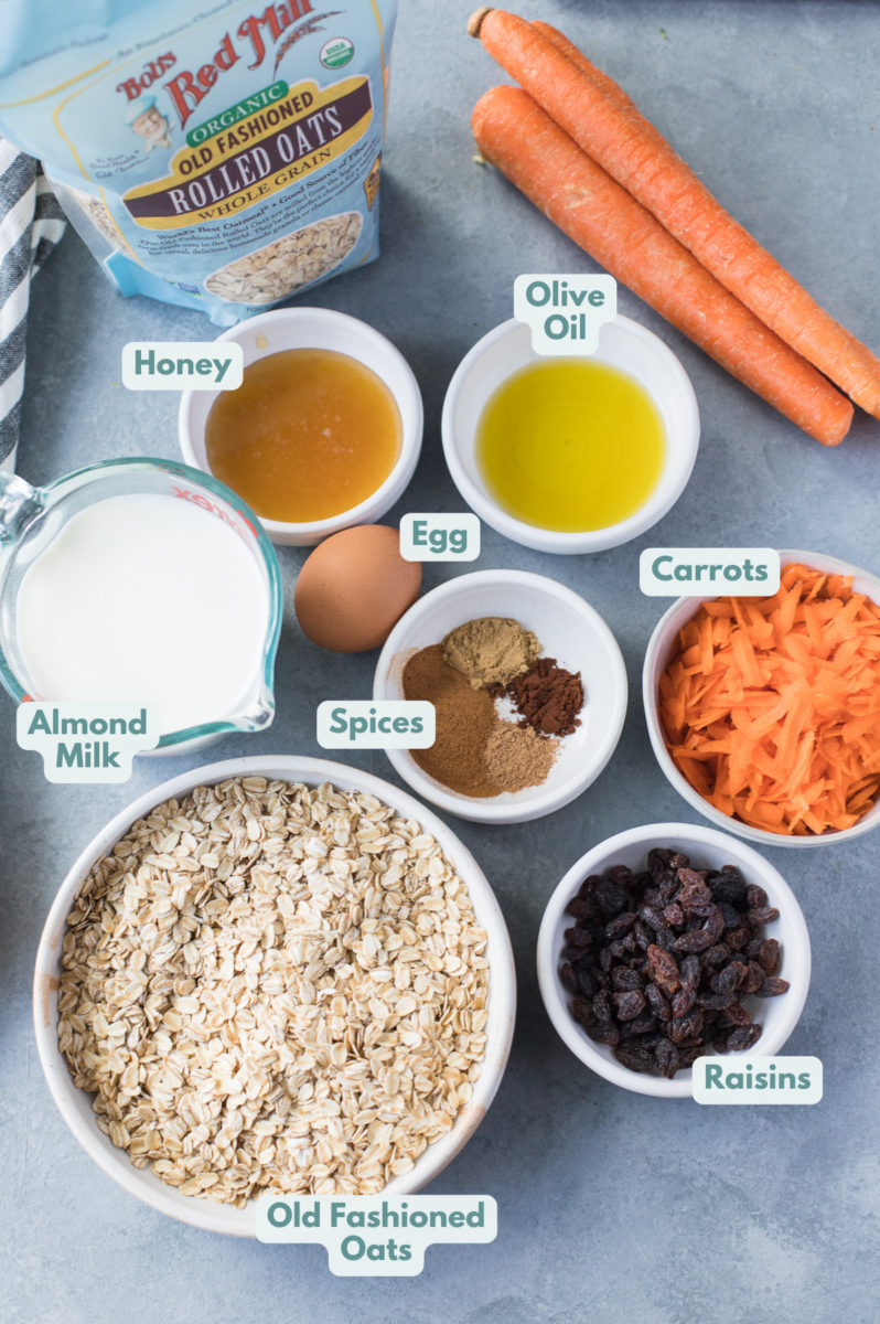 Ingredients for Carrot Cake Baked Oatmeal in small white bowls: oats, milk, egg, spices, raisins, carrots, olive oil, honey
