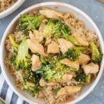 Easy Chicken and Broccoli Stir Fry in a white bowl on a grey background with a bowl and cutting board off to the side