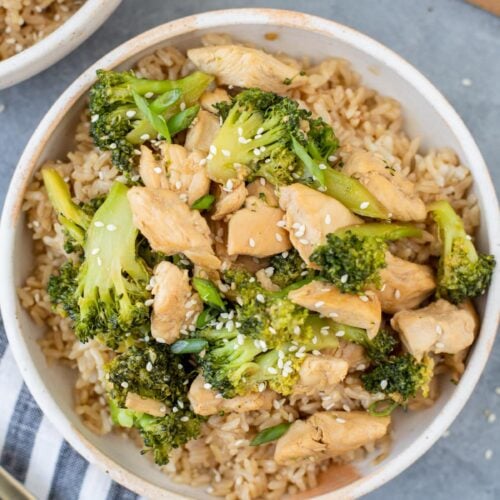 Easy Chicken and Broccoli Stir Fry in a white bowl on a grey background with a bowl and cutting board off to the side