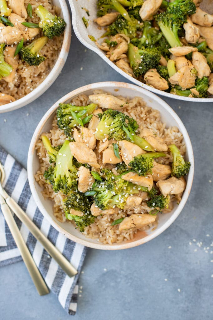 Two bowls of easy chicken and broccoli stir fry and a pan filled with stir fry off to the side