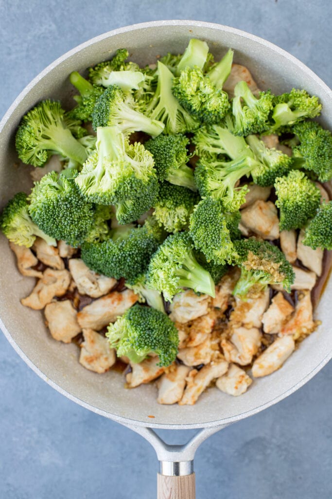 A grey pan with cooked chicken and raw broccoli piled on top of it