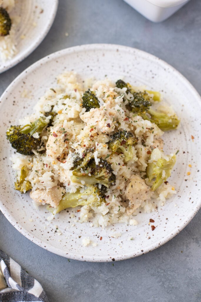 An overhead shot of cheesy chicken and rice casserole on a white plate on a grey background